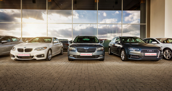 Fahrzeugleasing der Deutschen Leasing Diverse Autos stehen vor einem Glasgebäude der Deutsche Leasing